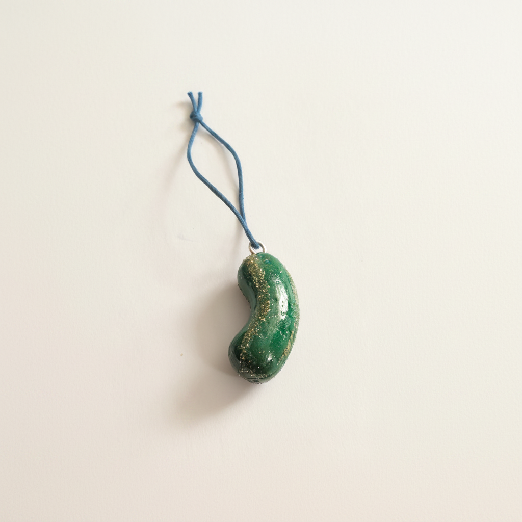 Handmade green pickle Christmas tree ornament on a soft ivory background