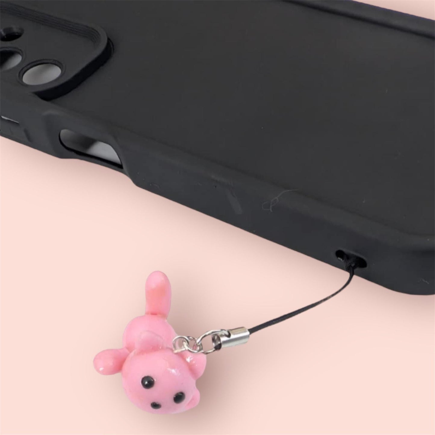 Pink phone charm attached to a black phone case on a light pink background