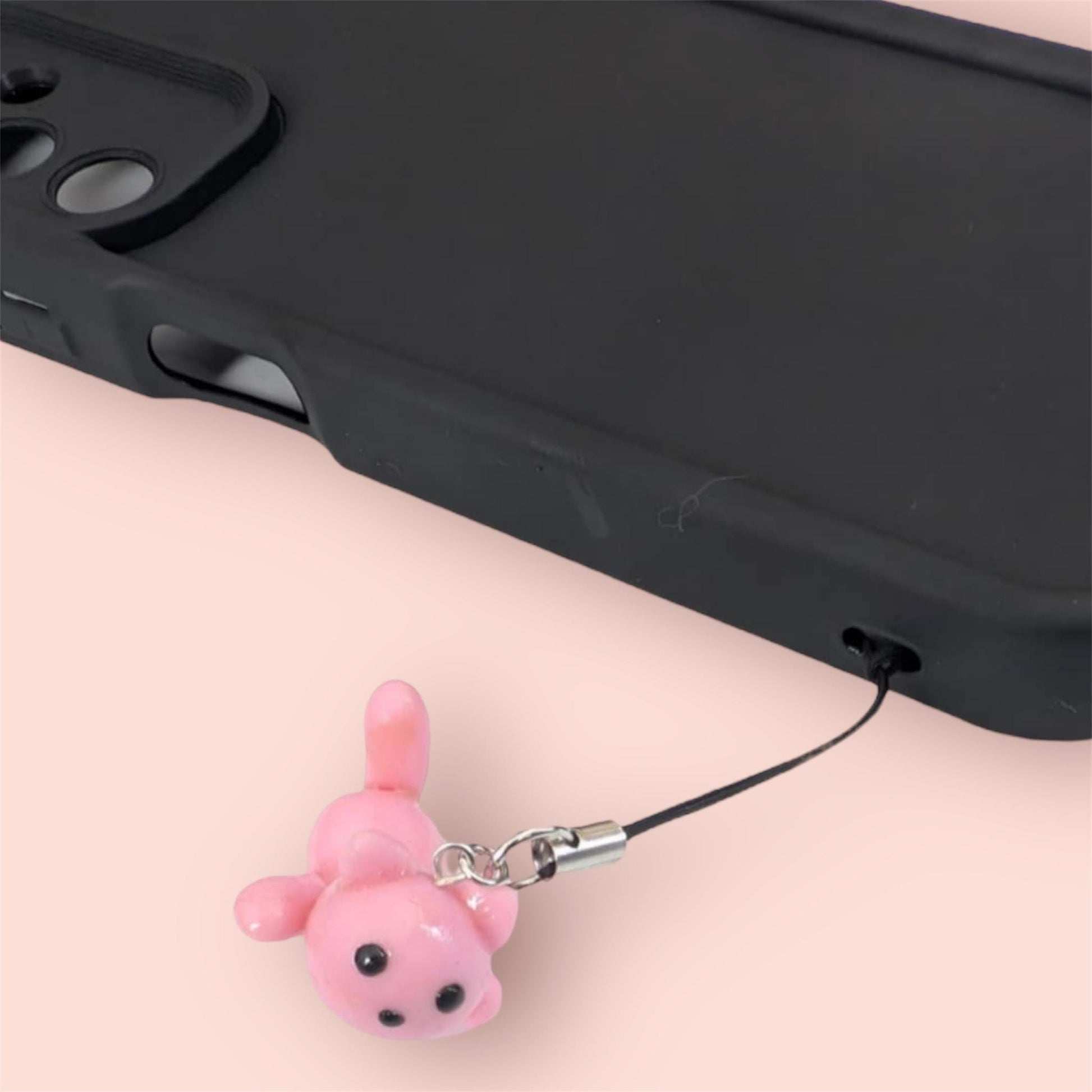 Pink phone charm attached to a black phone case on a light pink background