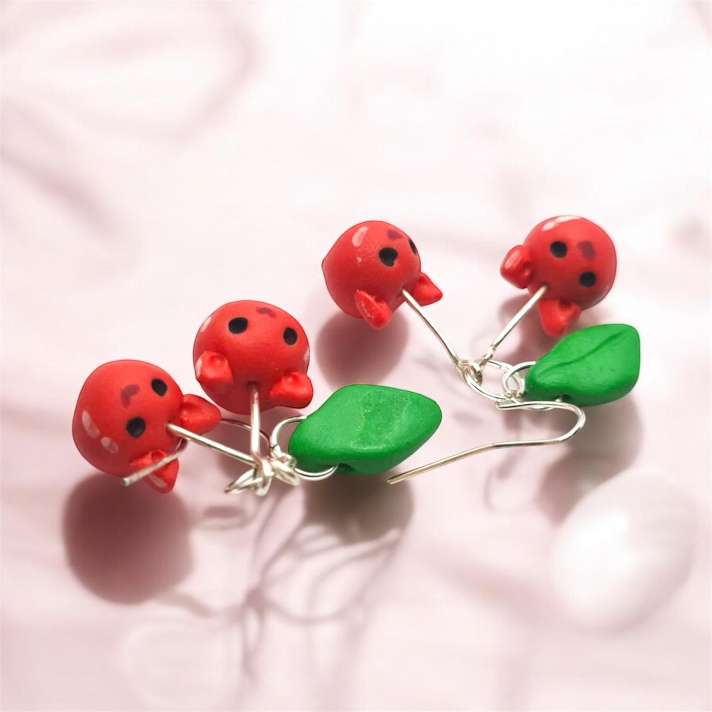 Red cat cherry earrings with green leaves on a pink background