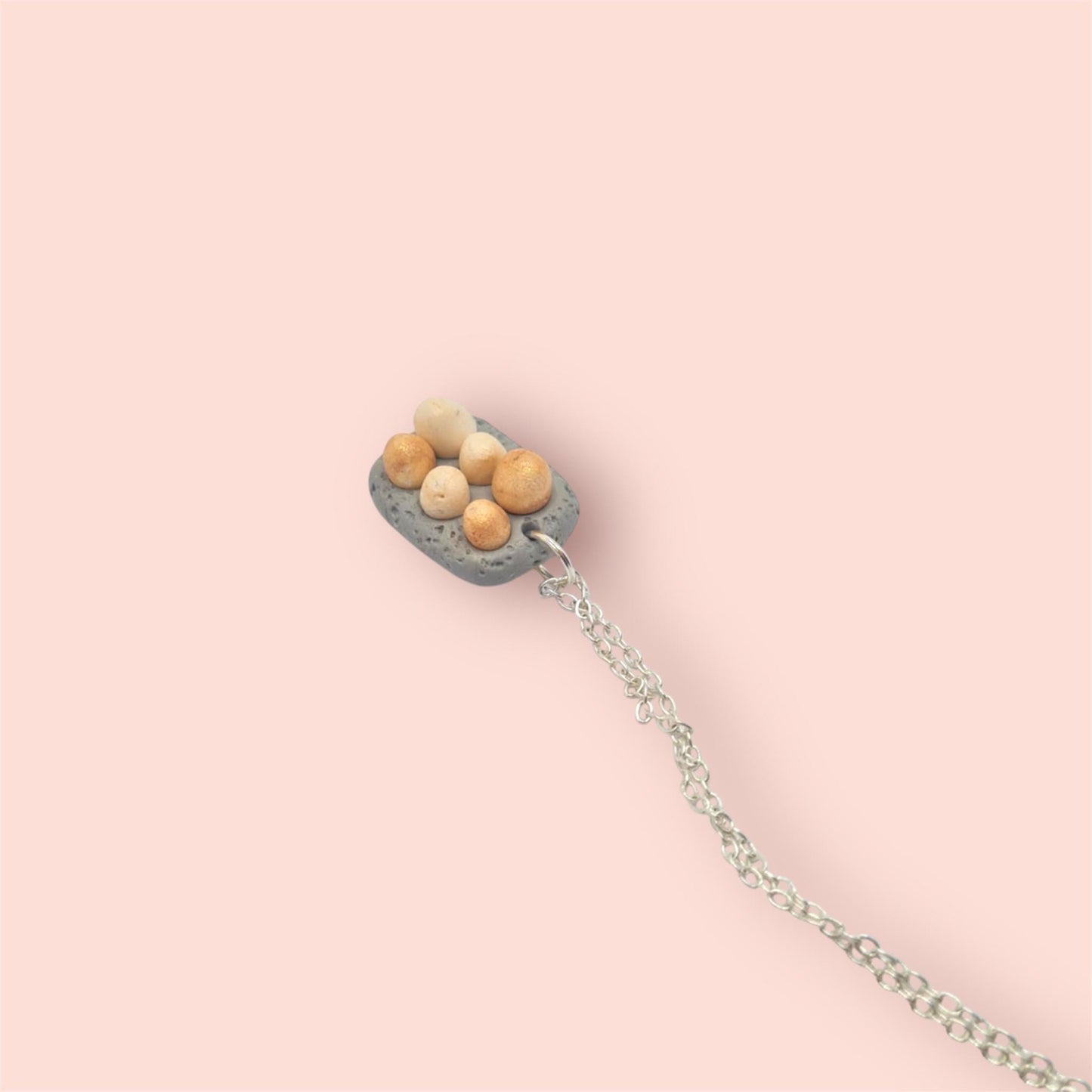 6 eggs in a grey carton pendant on a silver chain against a pink background 