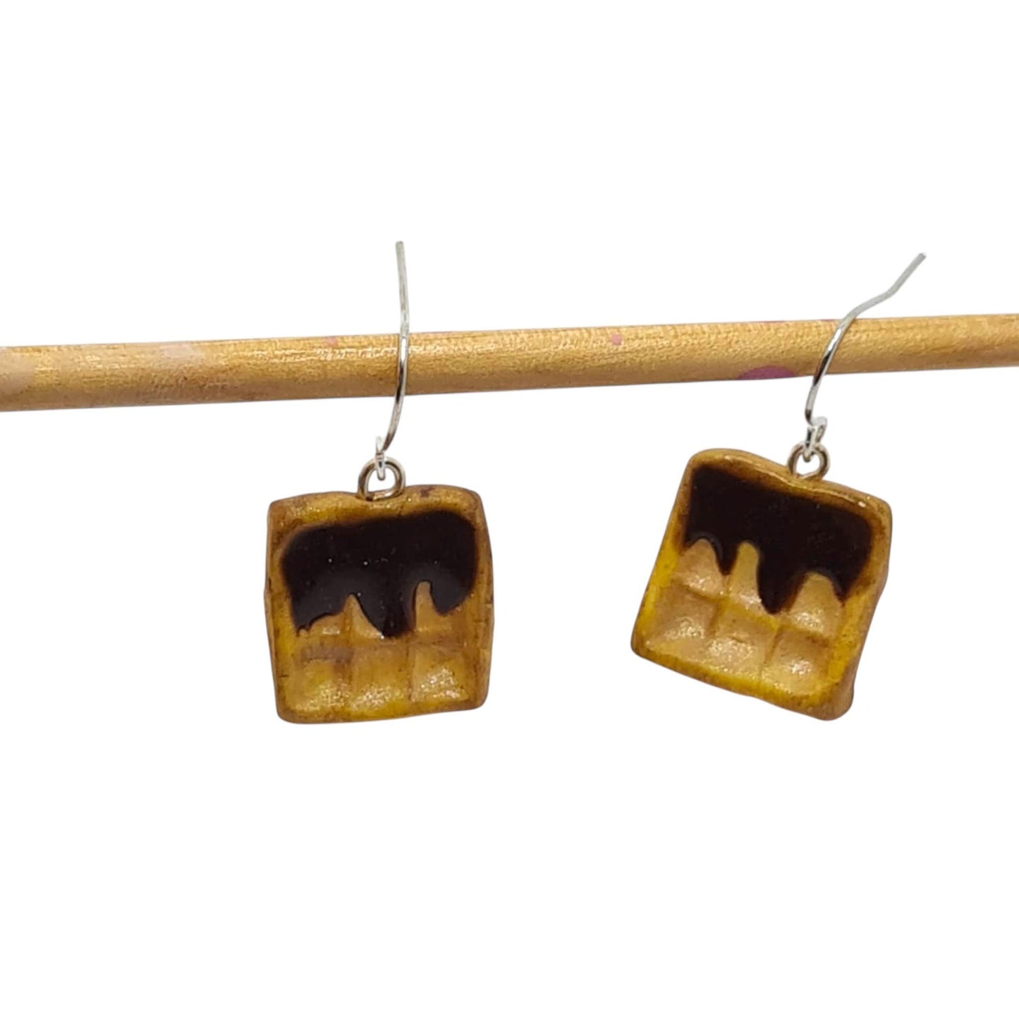 Square earrings with a brown and black design on a wooden stick against a white background