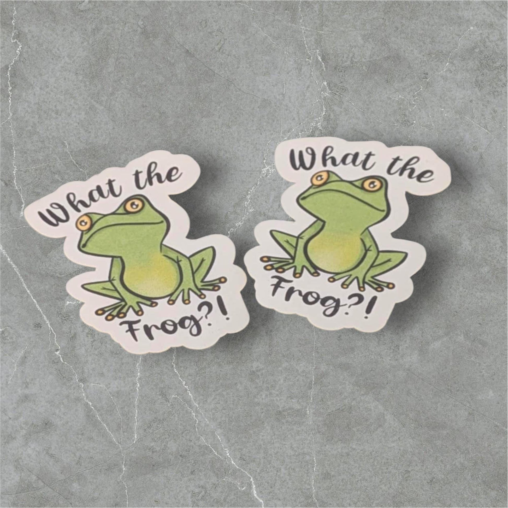 Two stickers with a frog design and 'What the Frog?!' text on a gray background.