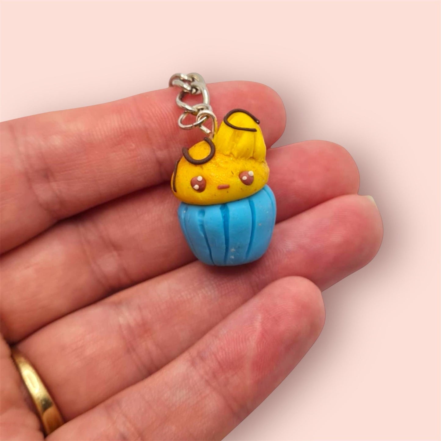 Cake shaped keychain with a face held between fingers on a light pink background