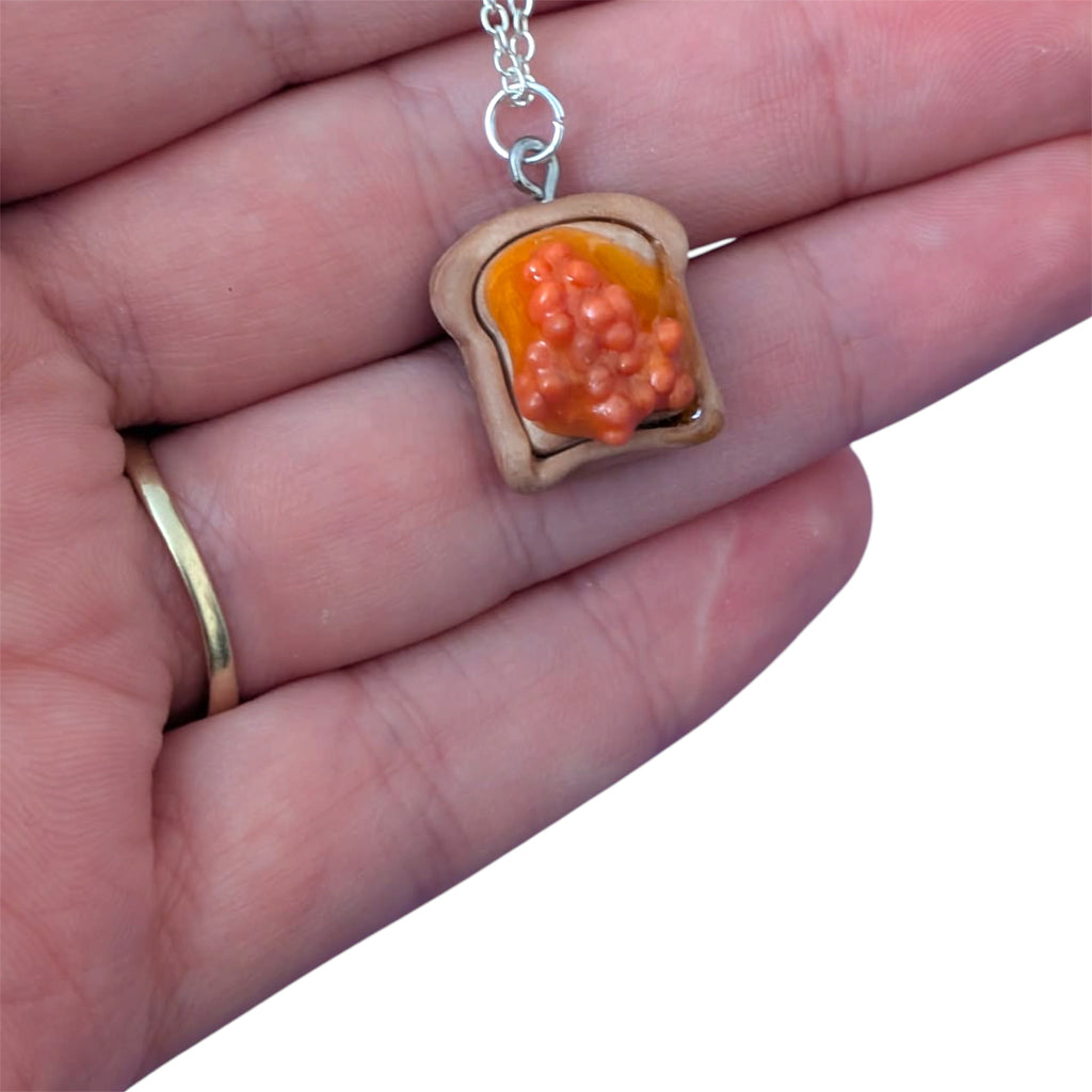 Hand holding beans on toast pendant with orange beans made with resin 