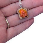 Hand holding beans on toast pendant with orange beans made with resin 