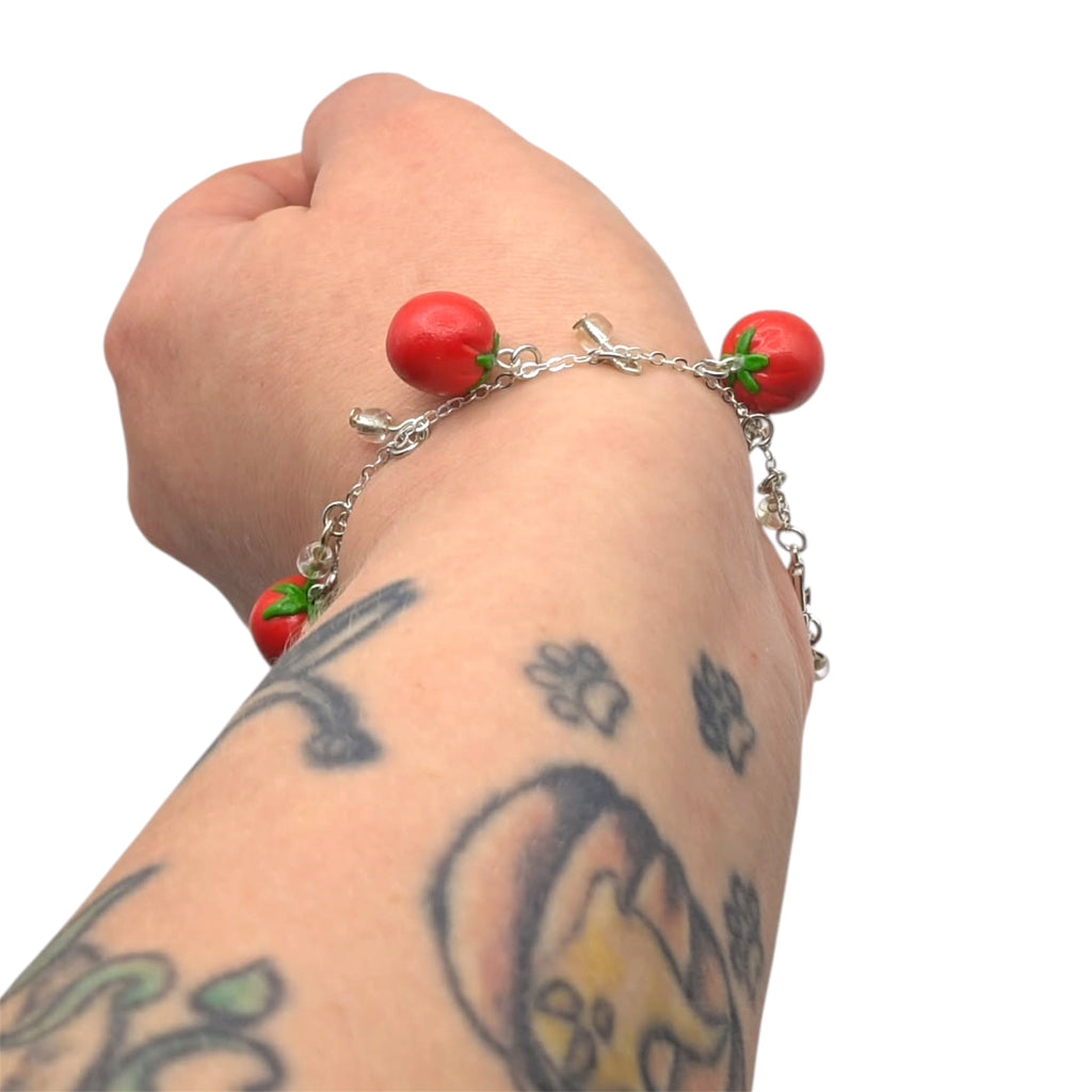 Bracelet with red tomato-shaped polymer clay charms on a wrist with tattoos