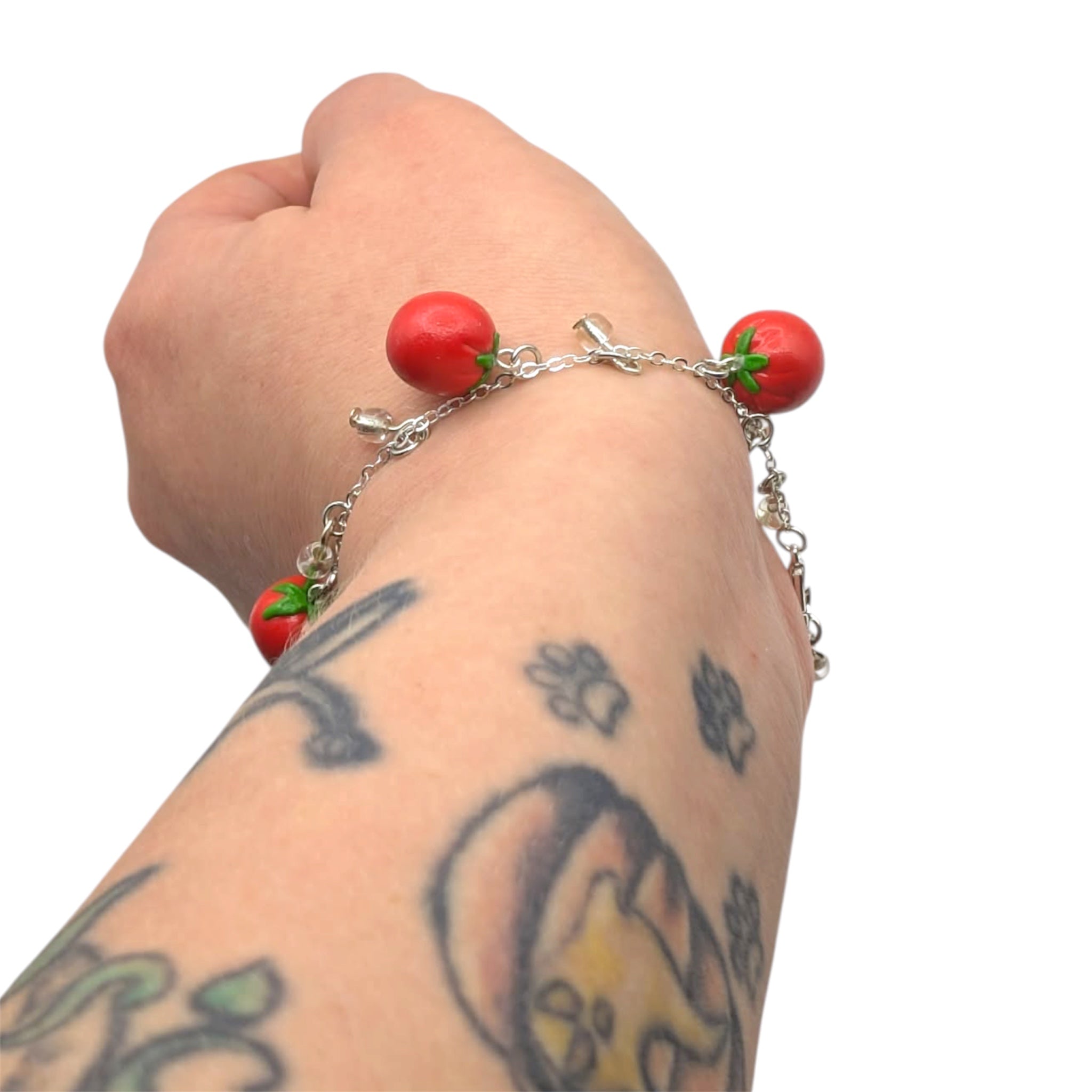 Bracelet with red tomato-shaped polymer clay charms on a wrist with tattoos