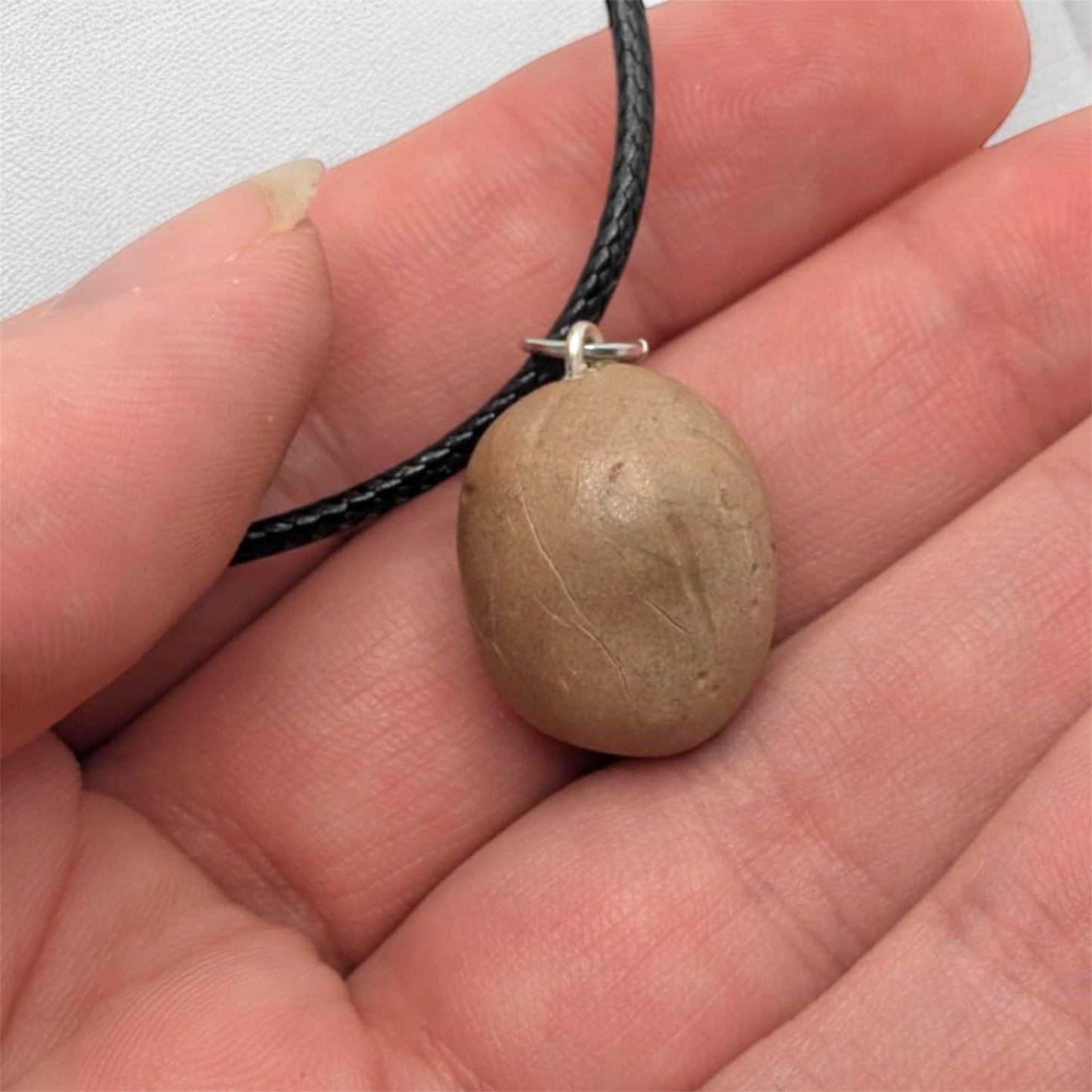 Hand holding a necklace showing the back of potato pendant and black cord.