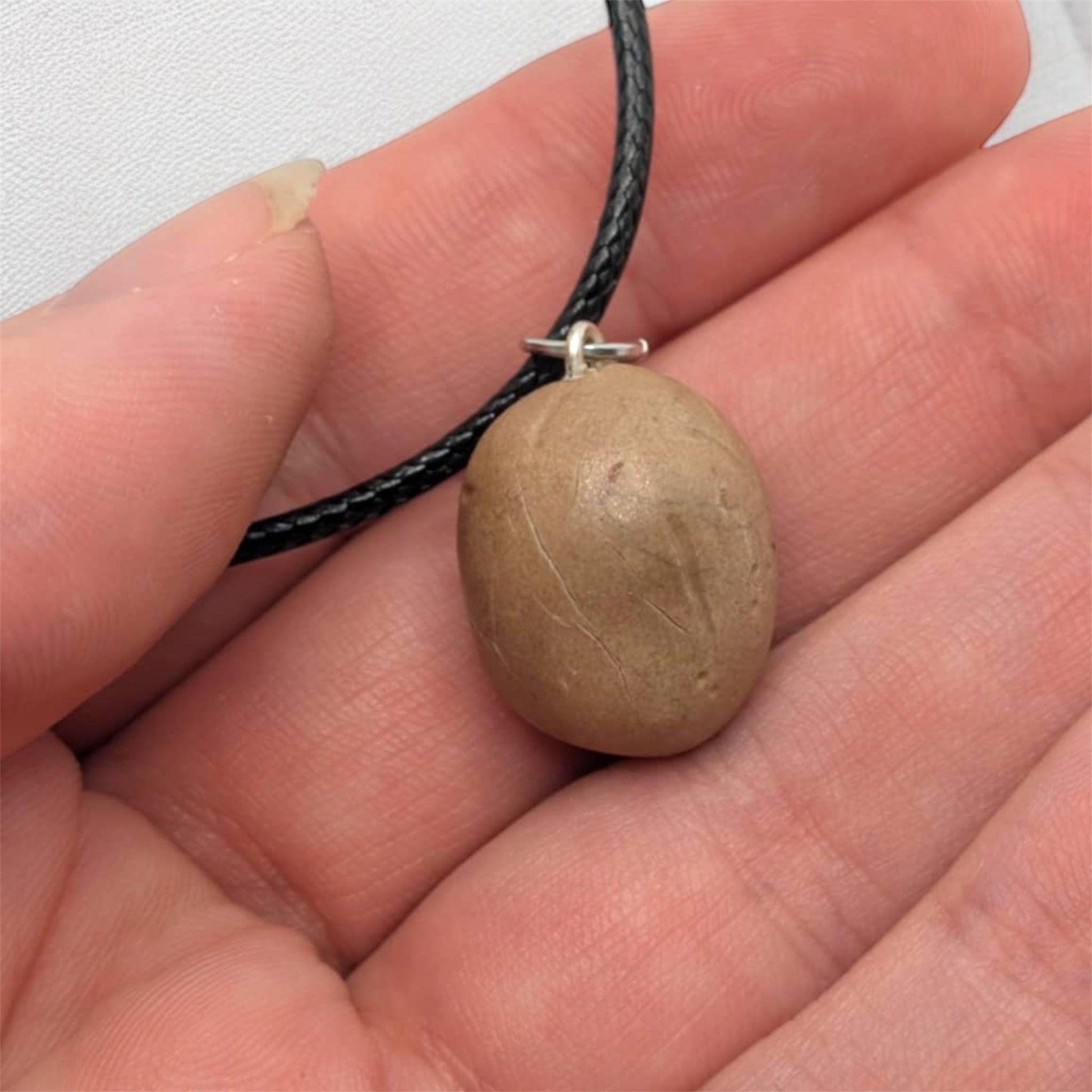 Hand holding a necklace showing the back of potato pendant and black cord.