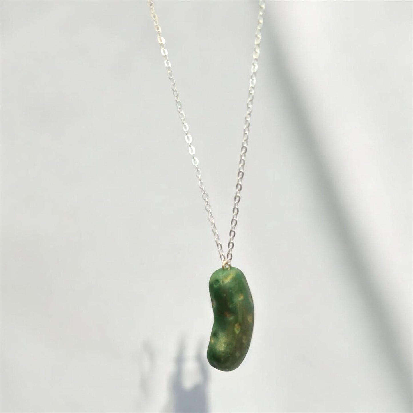 Green bean-shaped pendant on a silver chain against a white background
