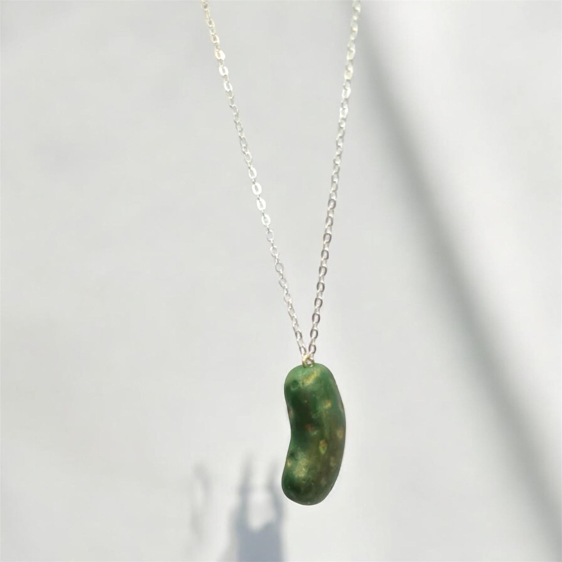 Green bean-shaped pendant on a silver chain against a white background