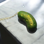 Green and yellow object resembling a pickle on a gold chain against a white background