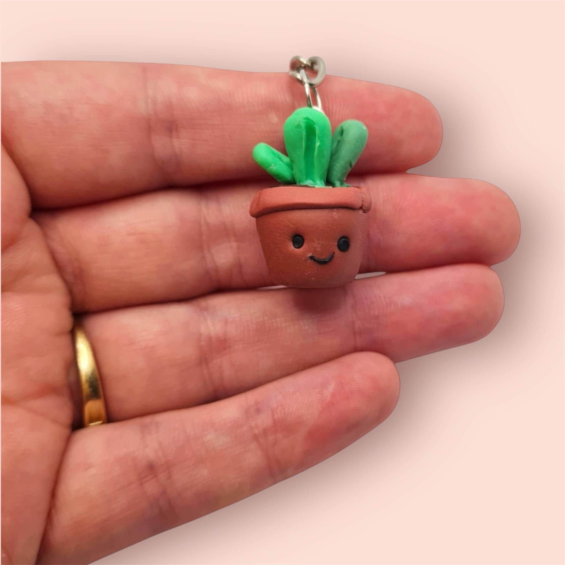 Small potted cactus charm held in a hand against a plain background