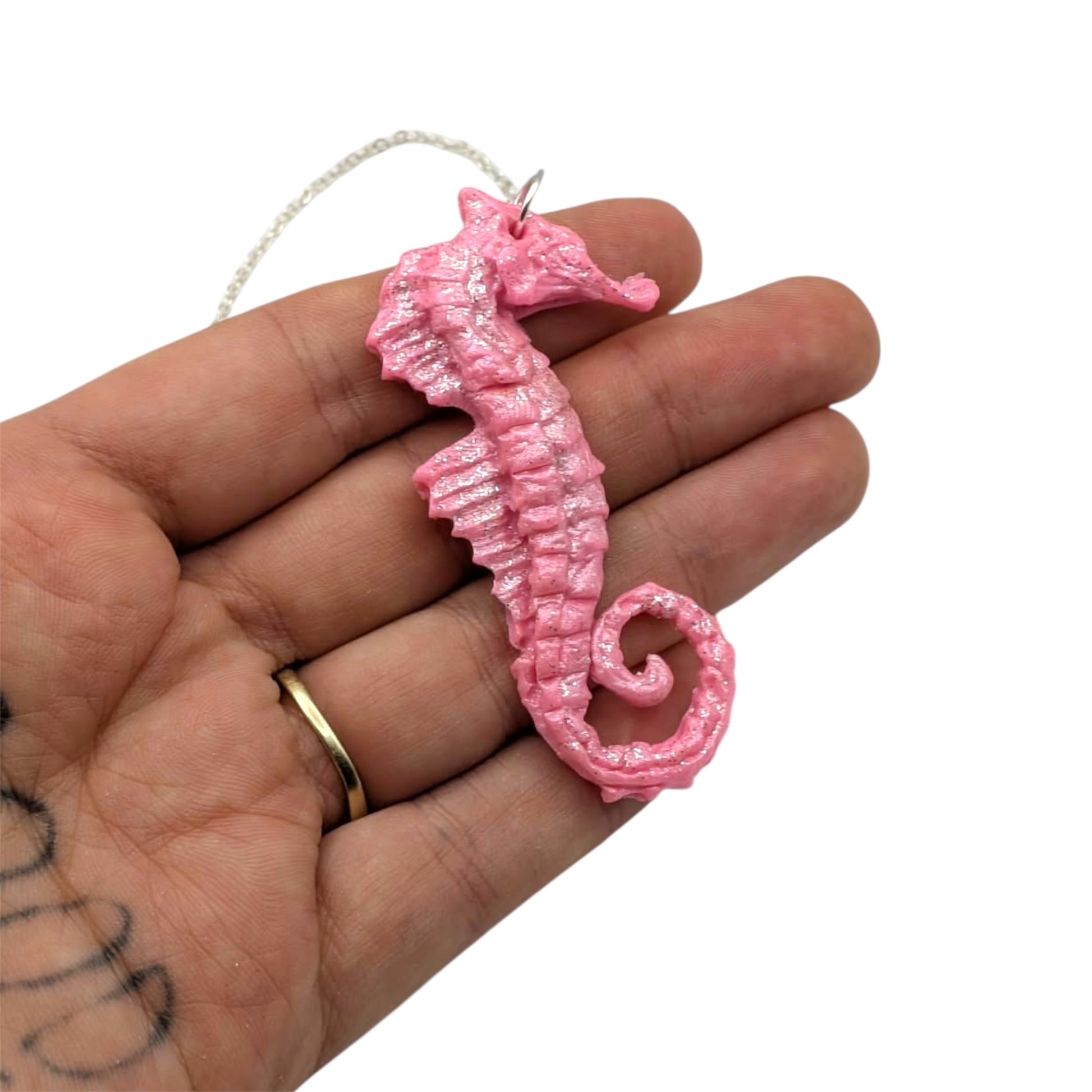 Pink sparkly seahorse necklace with pearl accent held in hand showing 6.5cm pendant size and texture