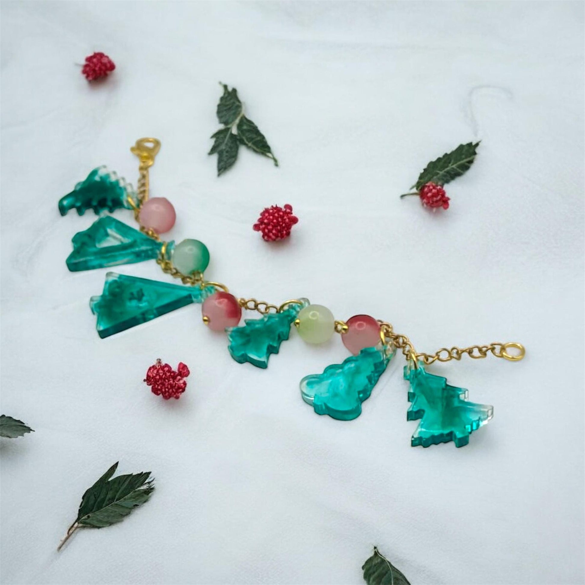 Bracelet with green tree-shaped pendants and red berries on a white background