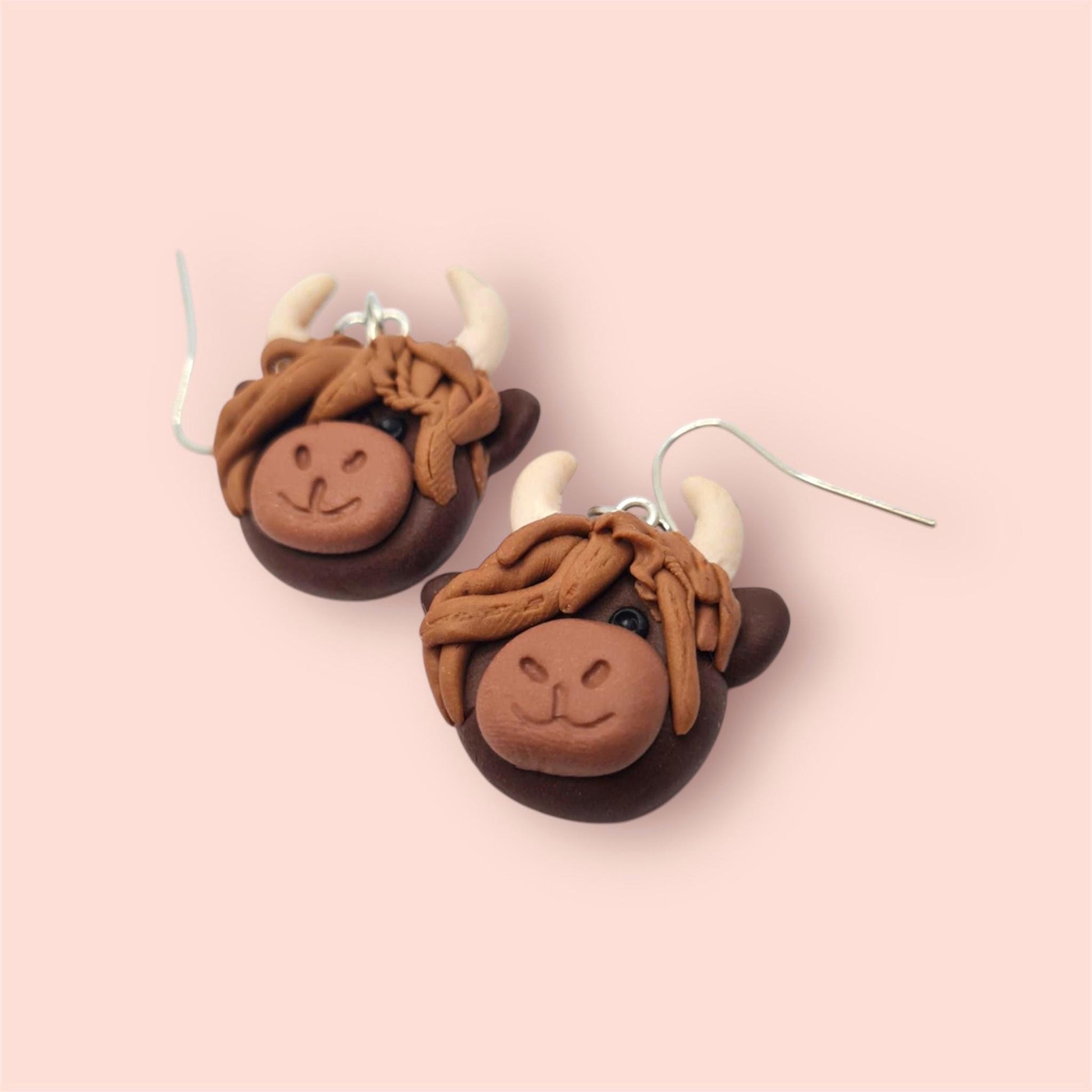 Pair of brown yak head earrings on a pink background