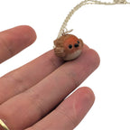 Tiny handmade robin bird pendant balanced on fingertip showing size