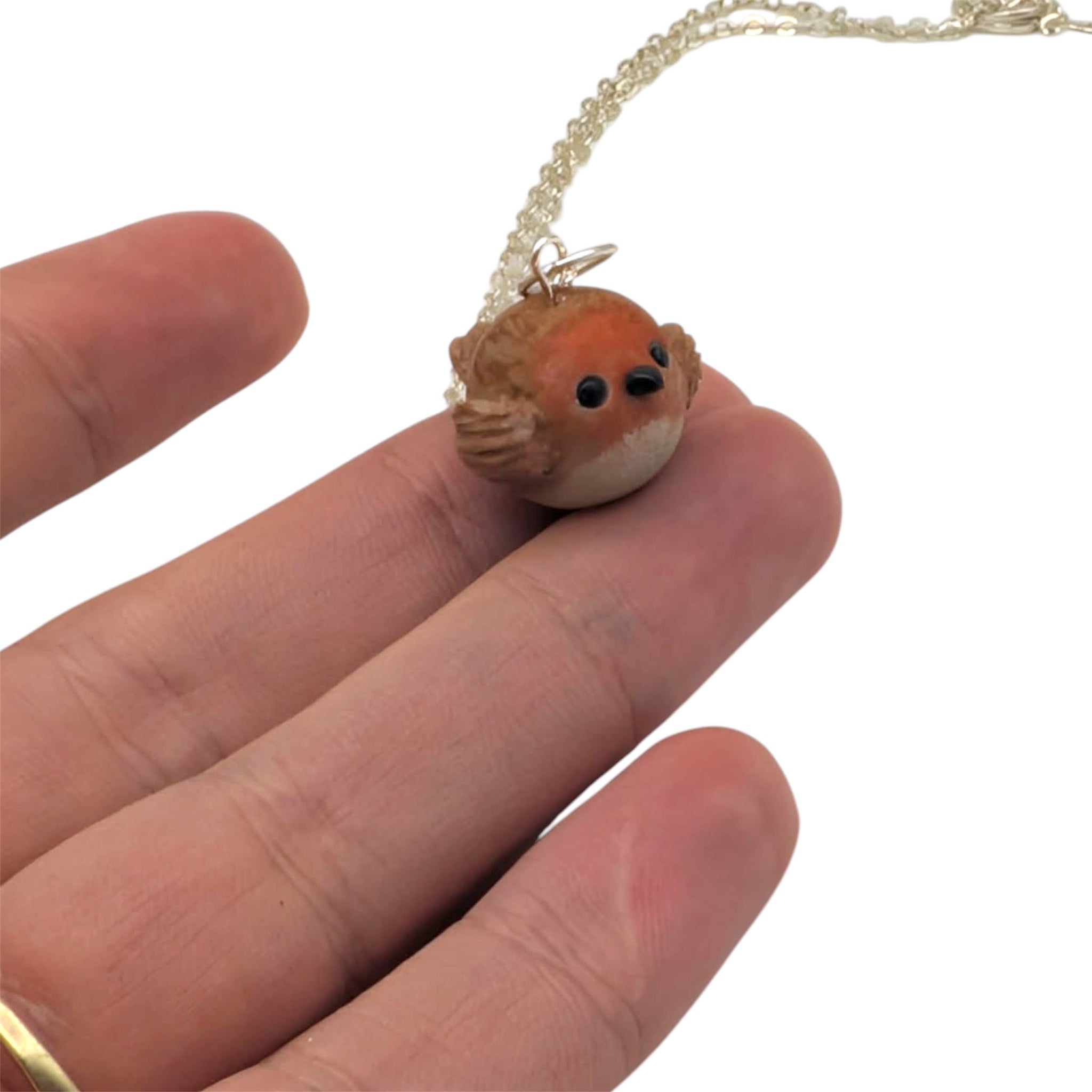 Tiny handmade robin bird pendant balanced on fingertip showing size
