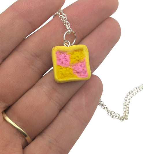 Yellow and pink square pendant on a silver chain held in a hand.