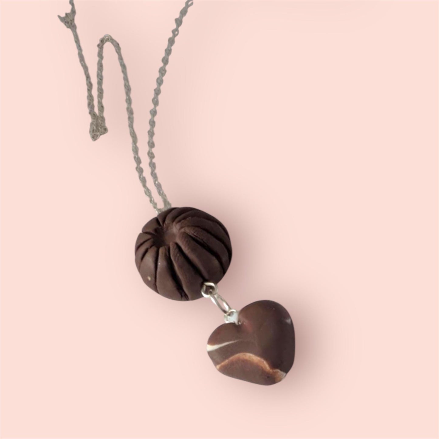 Necklace with heart-shaped and round brown pendant that look like chocolate's on a pink background
