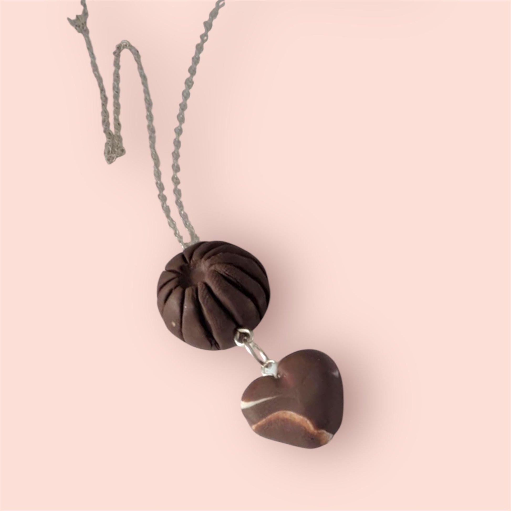 Necklace with heart-shaped and round brown pendant that look like chocolate's on a pink background