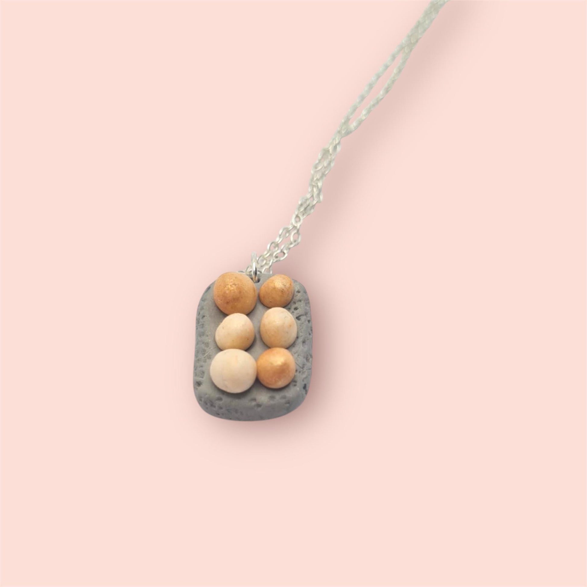 Necklace with a rectangular pendant featuring round eggs on a pink background