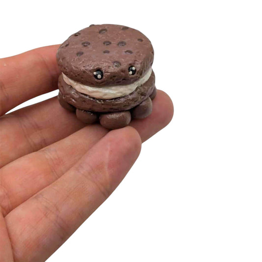 Small chocolate cookie with a white filling held in a hand against a white background