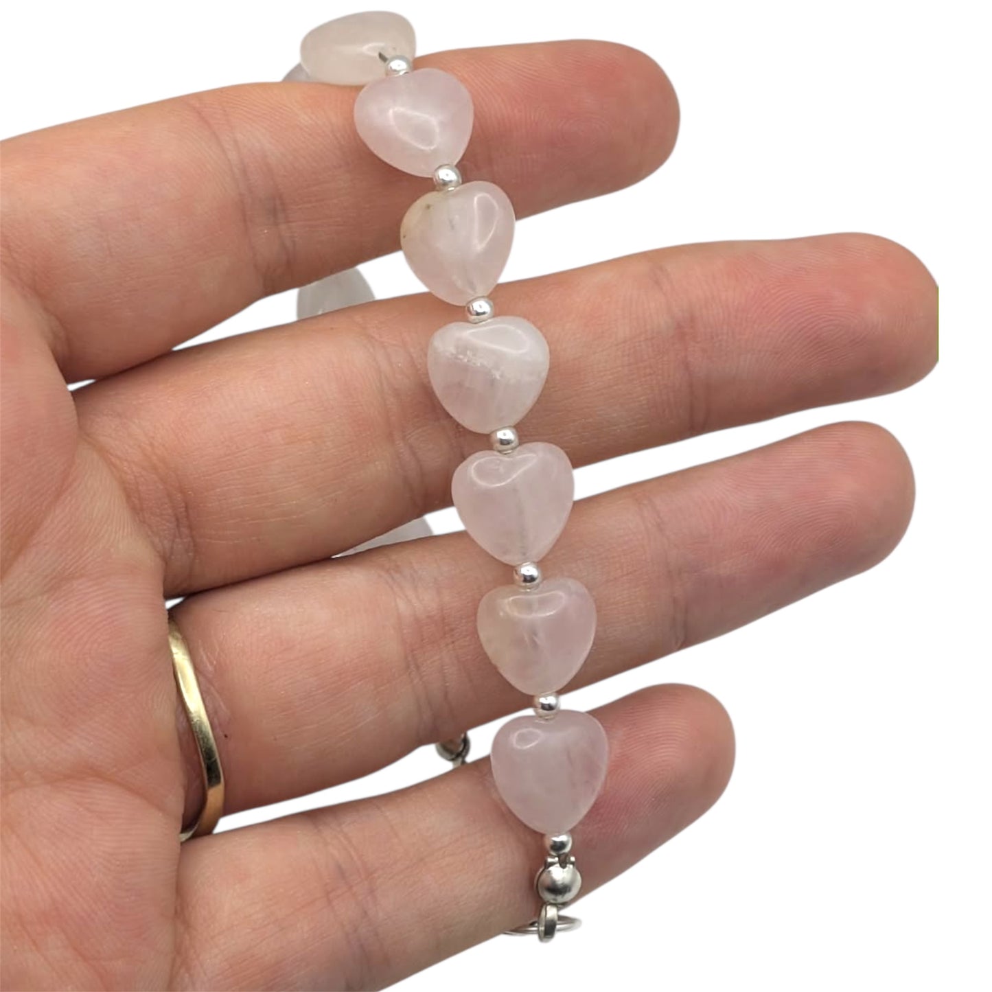 Handmade rose quartz heart bracelet with pink gemstone beads and silver chain held in hand on white background