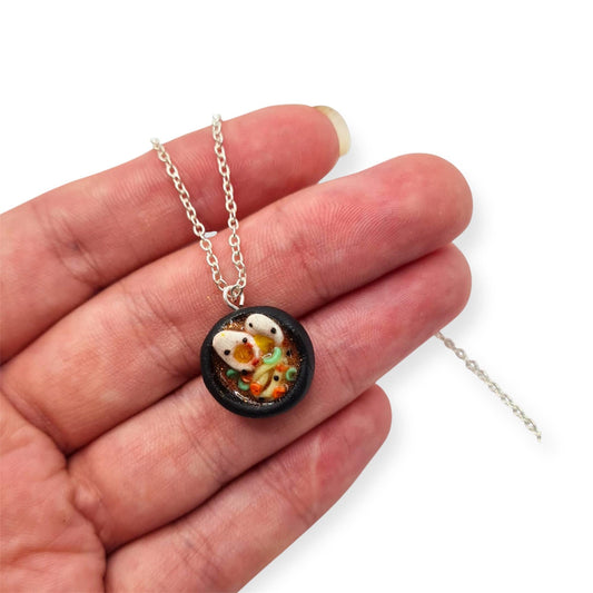 Necklace with a pendant featuring noodle soup character in a bowl held over fingers on a white background