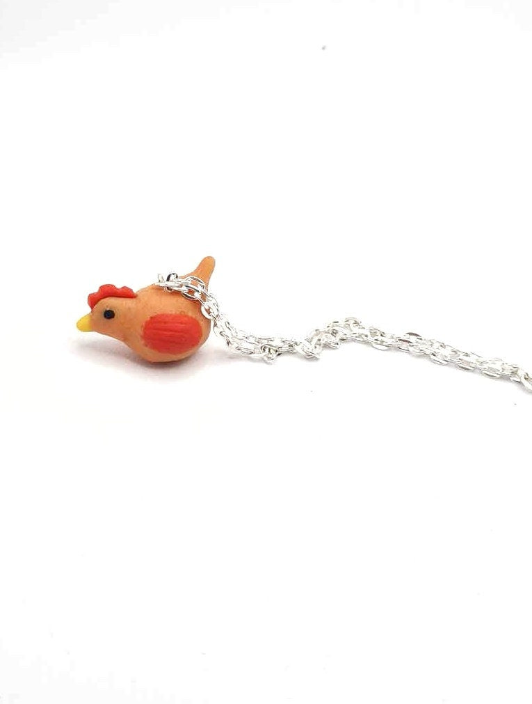 Small orange chicken-shaped pendant on a silver chain against a white background