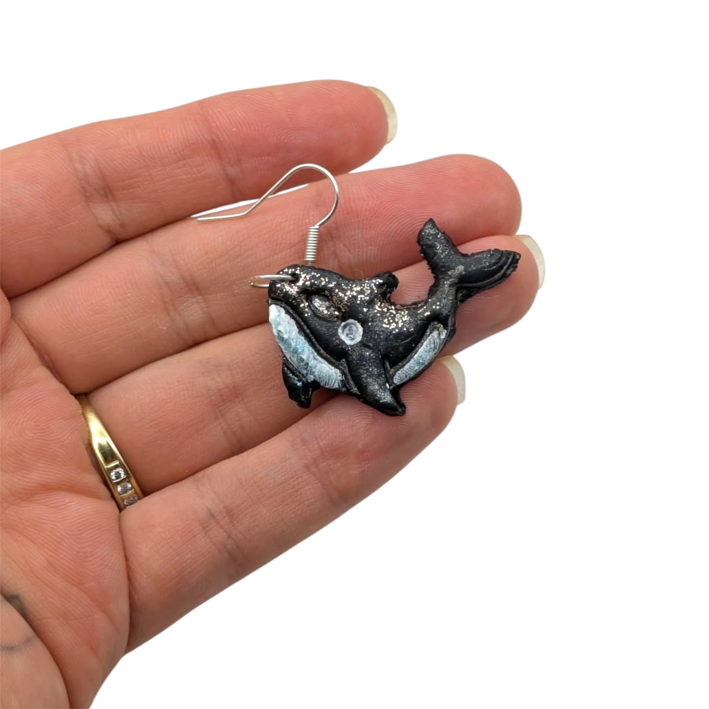 Orca whale-shaped earring held in a hand on a white background
