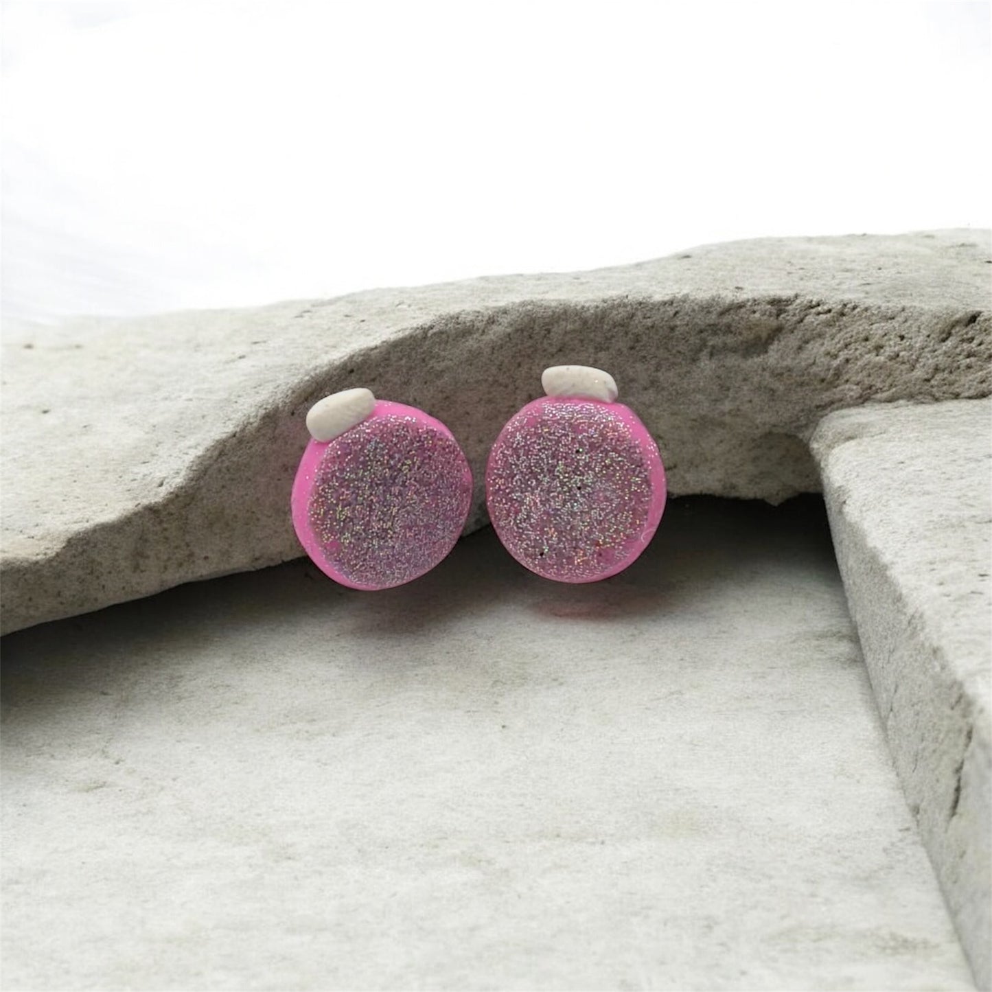 Pink glittery round earrings on a stone surface