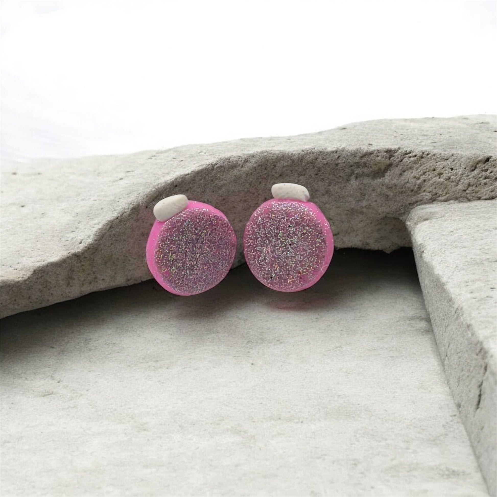 Pink glittery round earrings on a stone surface