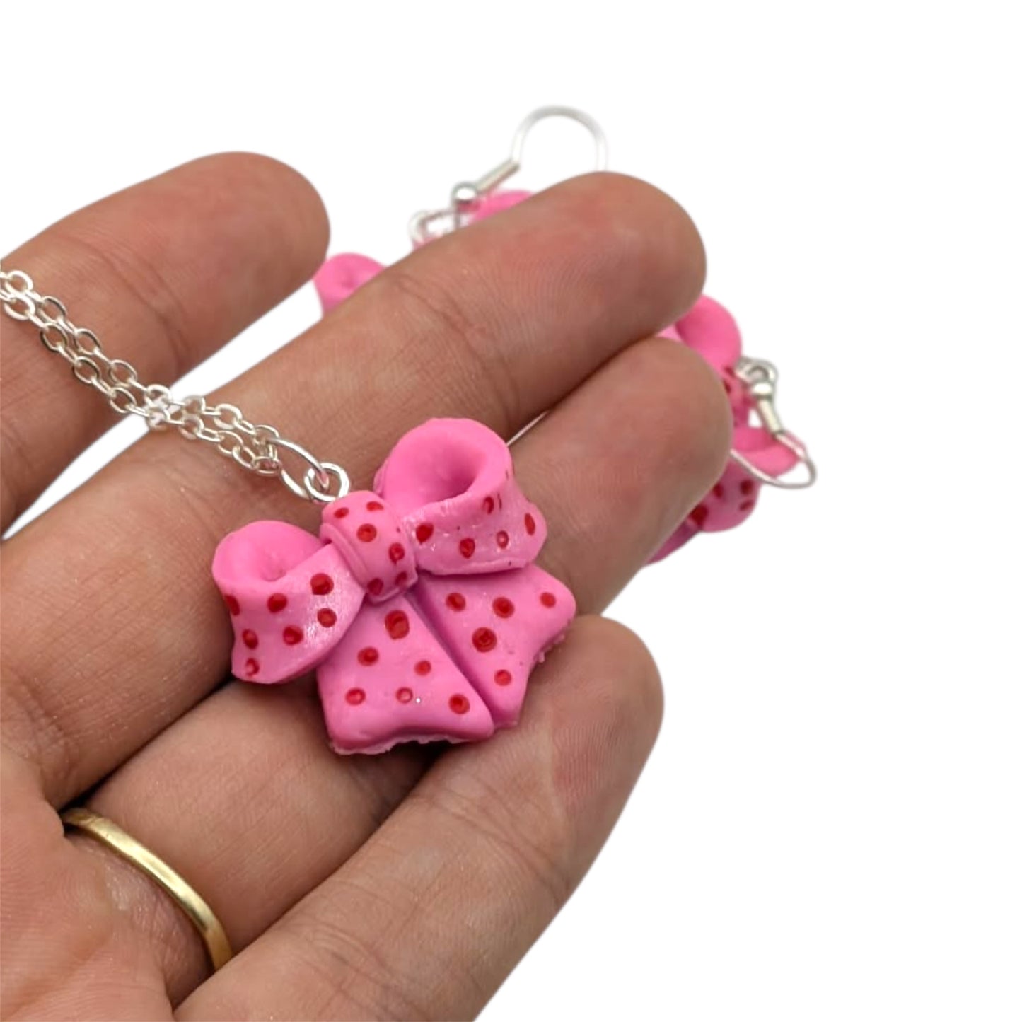 Pink bow with red dots on silver chain held in hand 