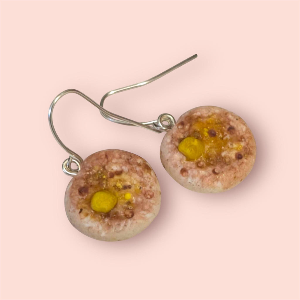 Round crumpet earrings with yellow center and brownish texture on a pink background