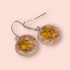 Round crumpet earrings with yellow center and brownish texture on a pink background