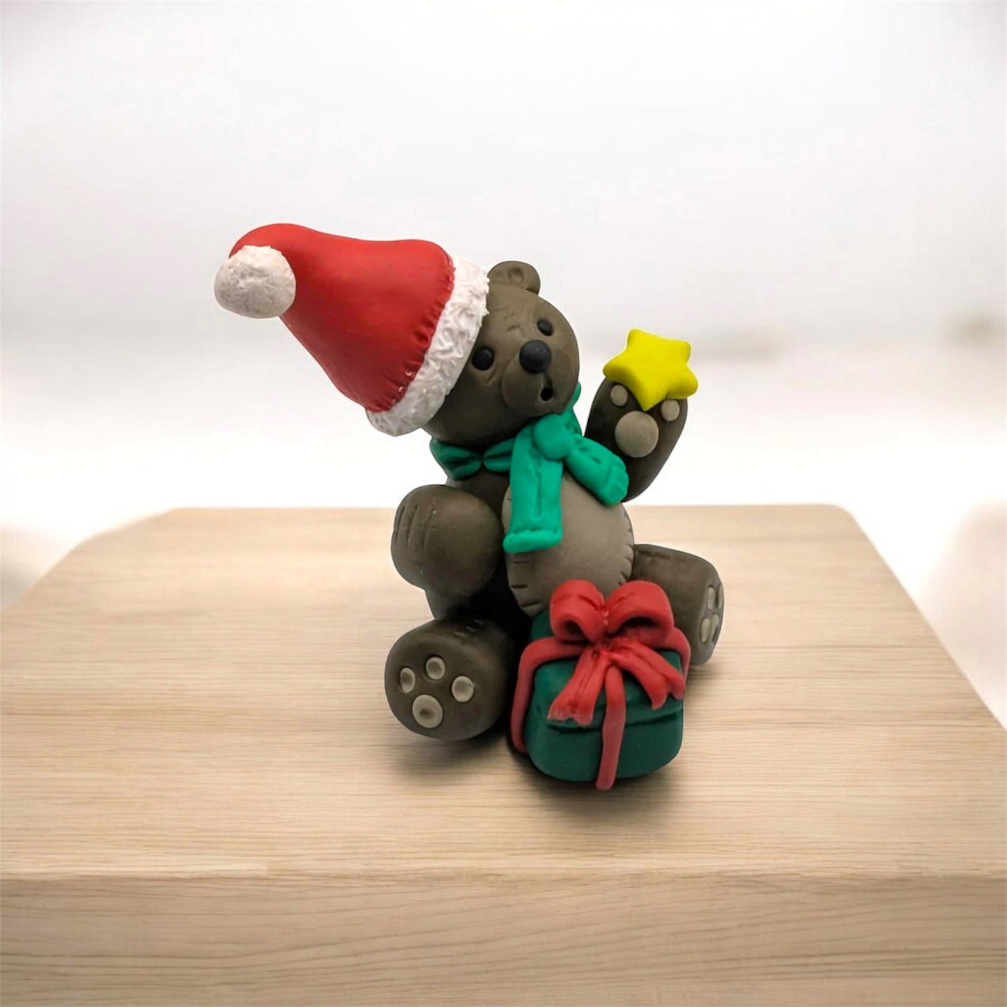 Festive teddy bear figurine with a Santa hat, green scarf, and red bow on a wooden surface.