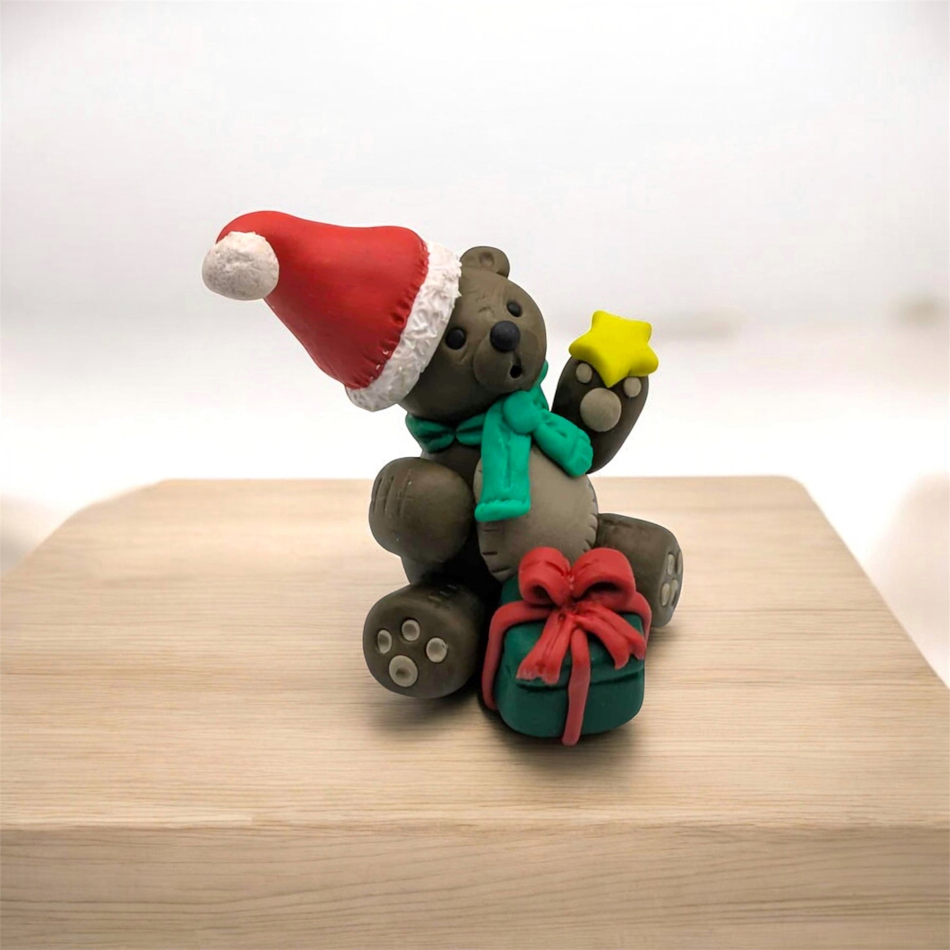 Festive teddy bear figurine with a Santa hat, green scarf, and red bow on a wooden surface.