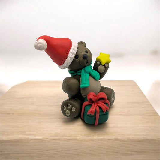 Festive teddy bear figurine with a Santa hat, green scarf, and red bow on a wooden surface.