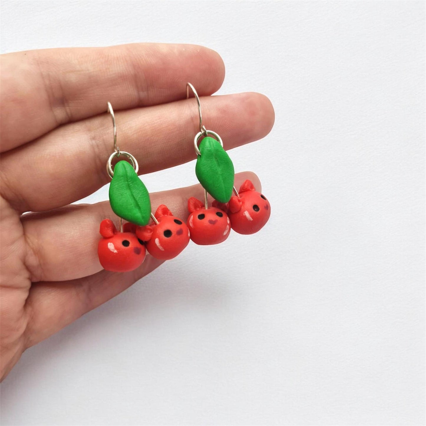 Hand holding a pair of earrings with red and green designs on a white background