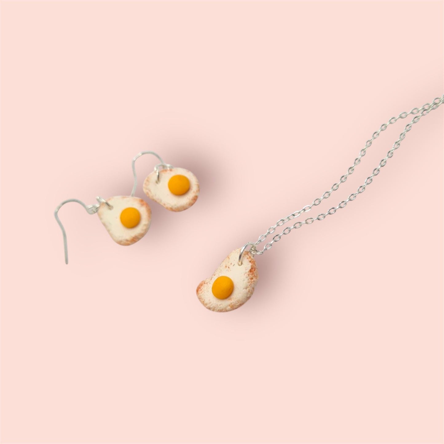 Egg-shaped earrings and necklace on a pink background