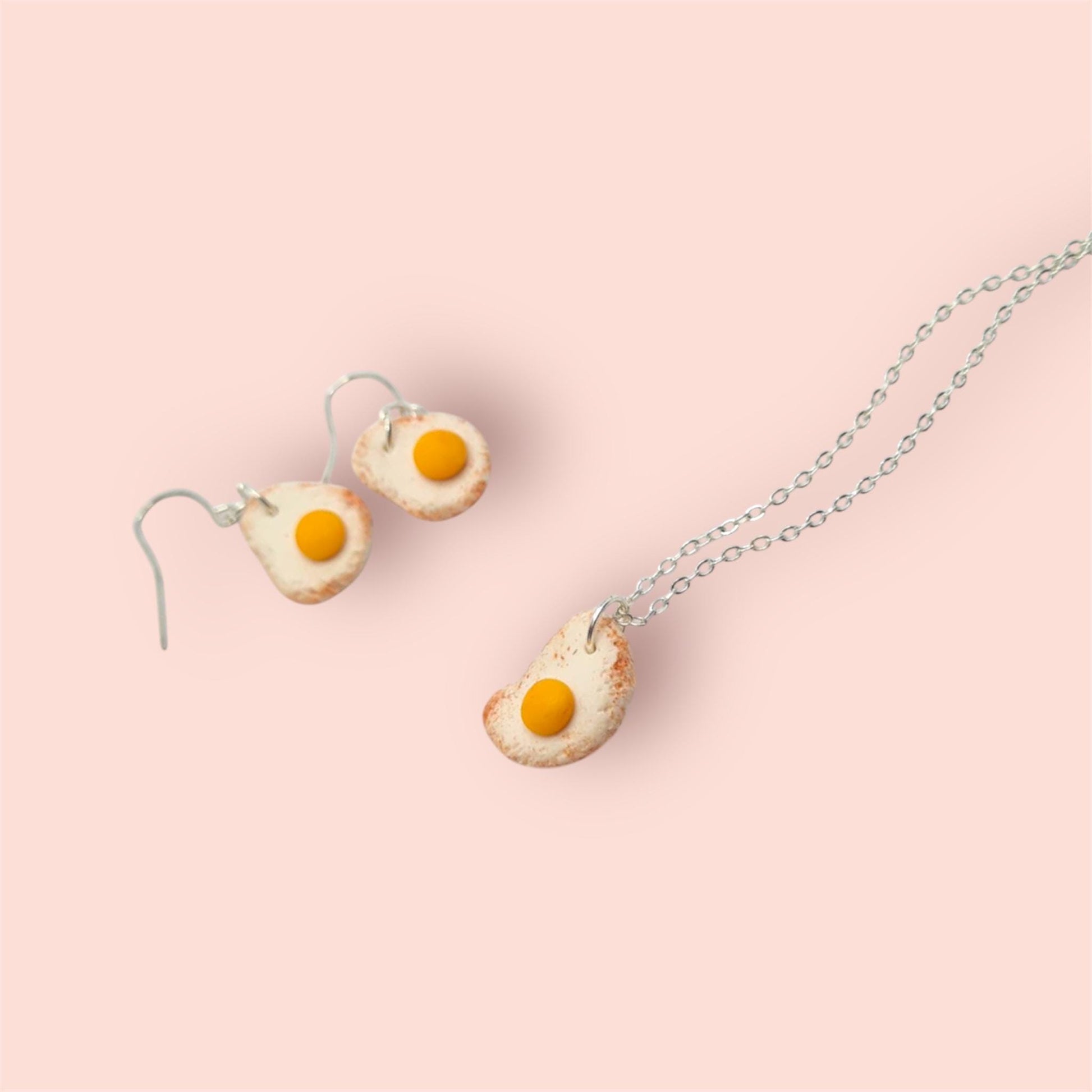 Egg-shaped earrings and necklace on a pink background