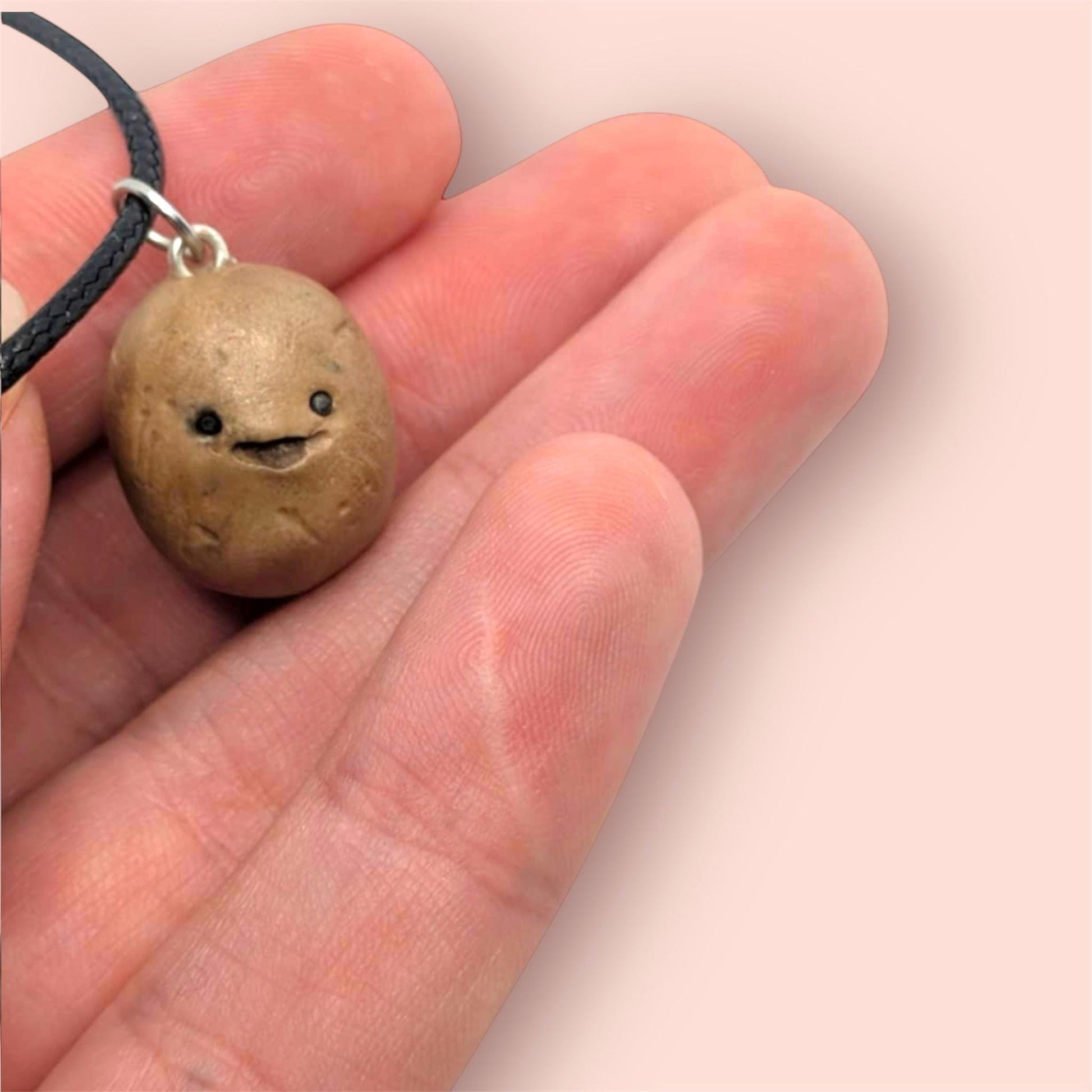 Hand holding a small round pendant with a smiling face design on a plain background