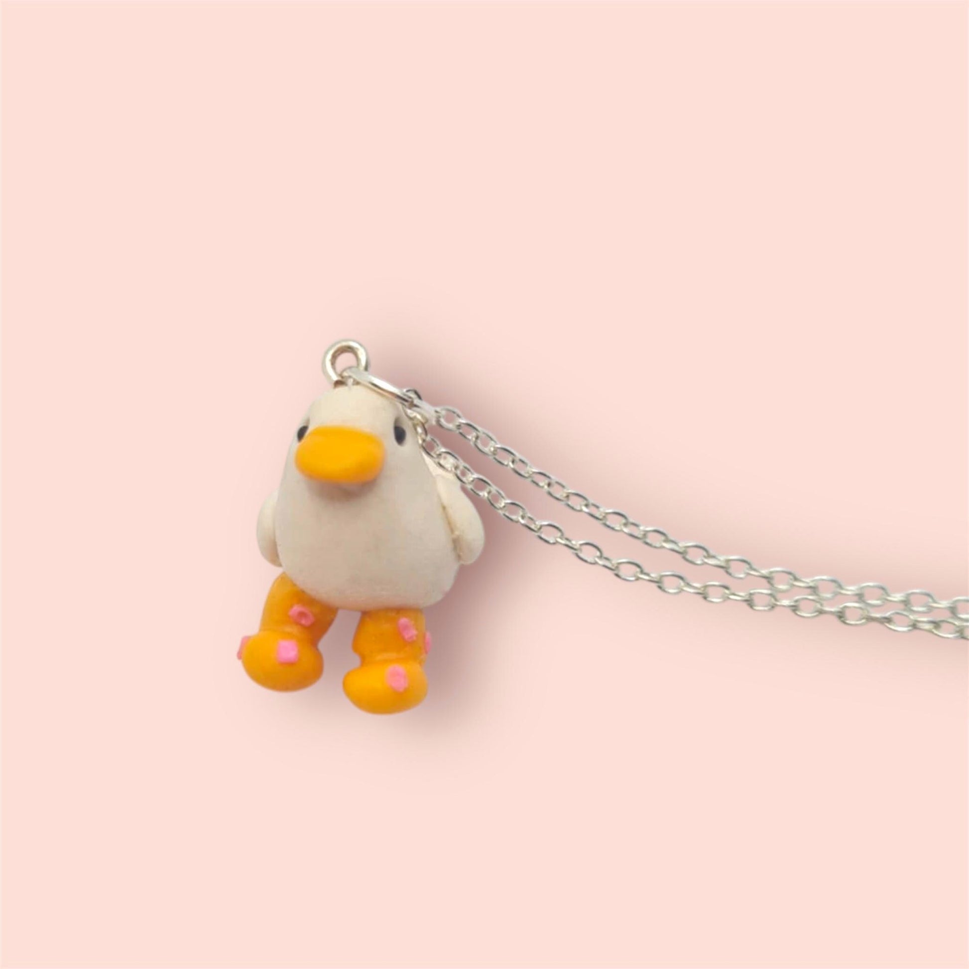 Small duck-shaped pendant on a chain against a light pink background