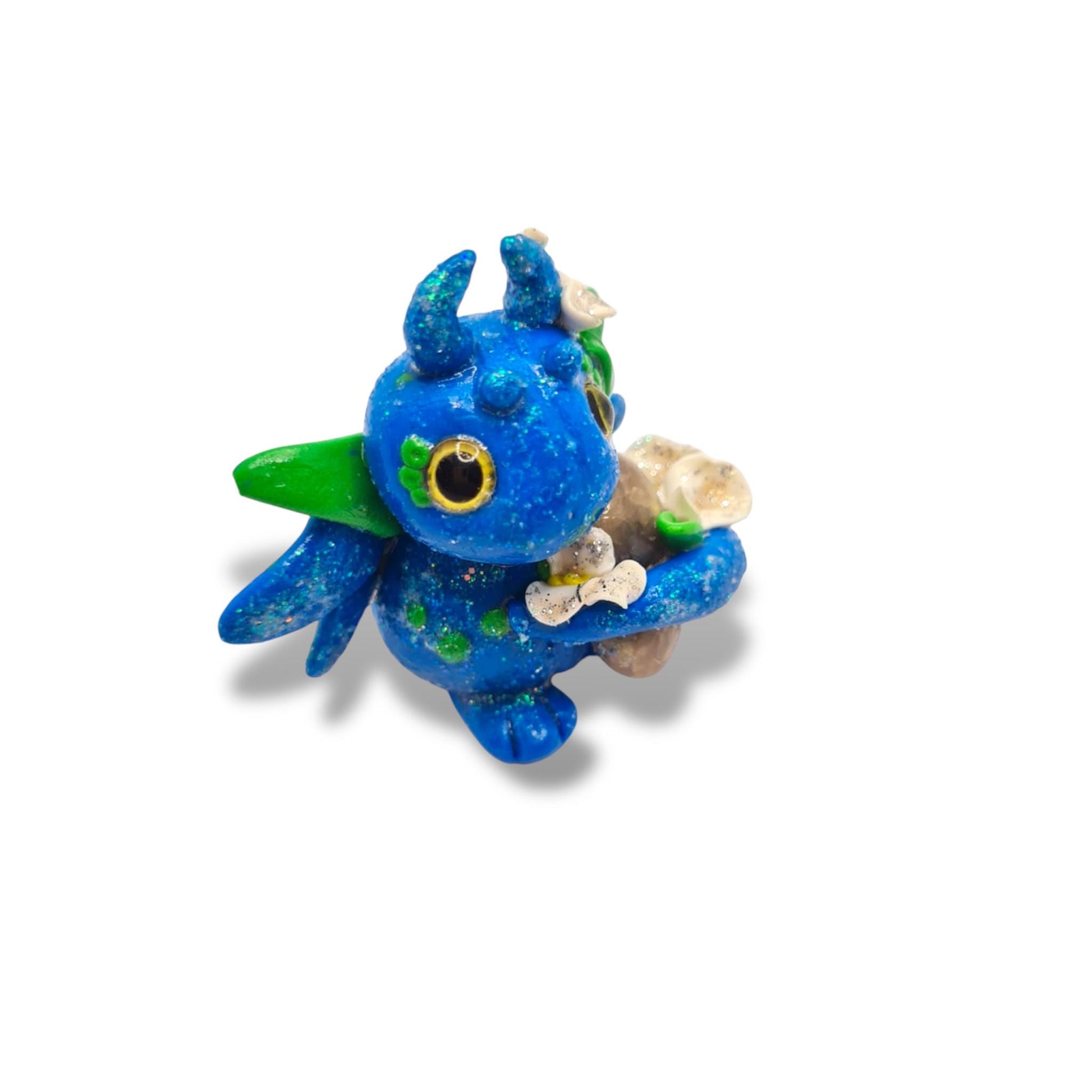Blue dragon figurine with green wings holding a shell on a white background