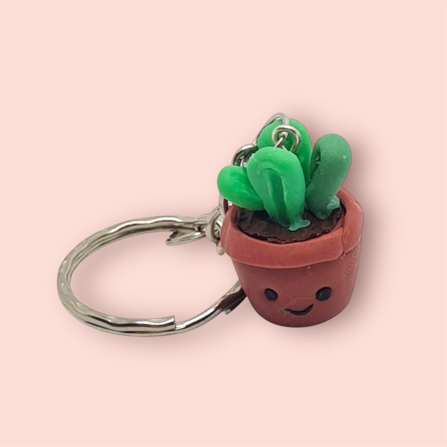 Cute potted plant keychain with a smiling face on a pink background