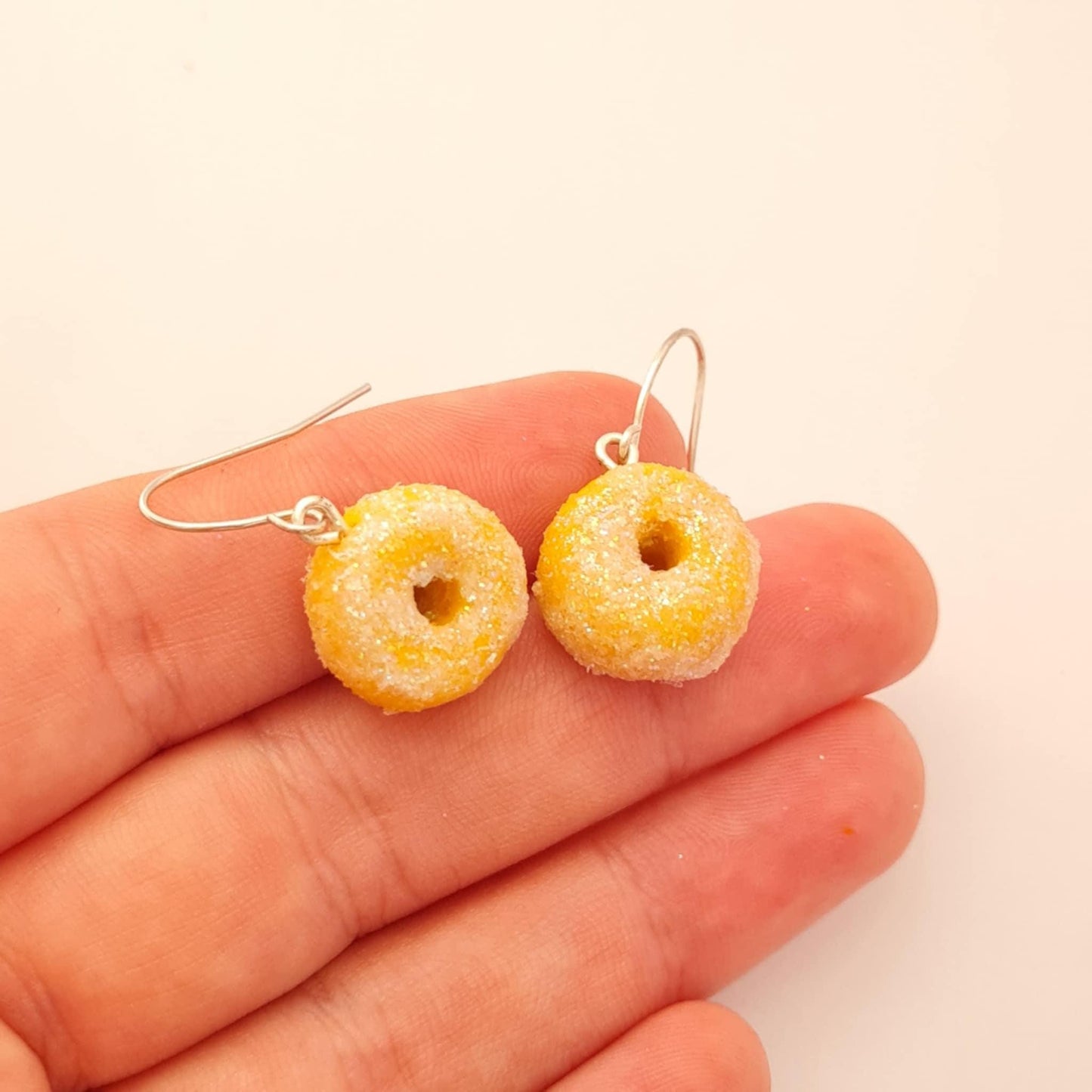 Yellow donut-shaped earrings held between fingers on a light background