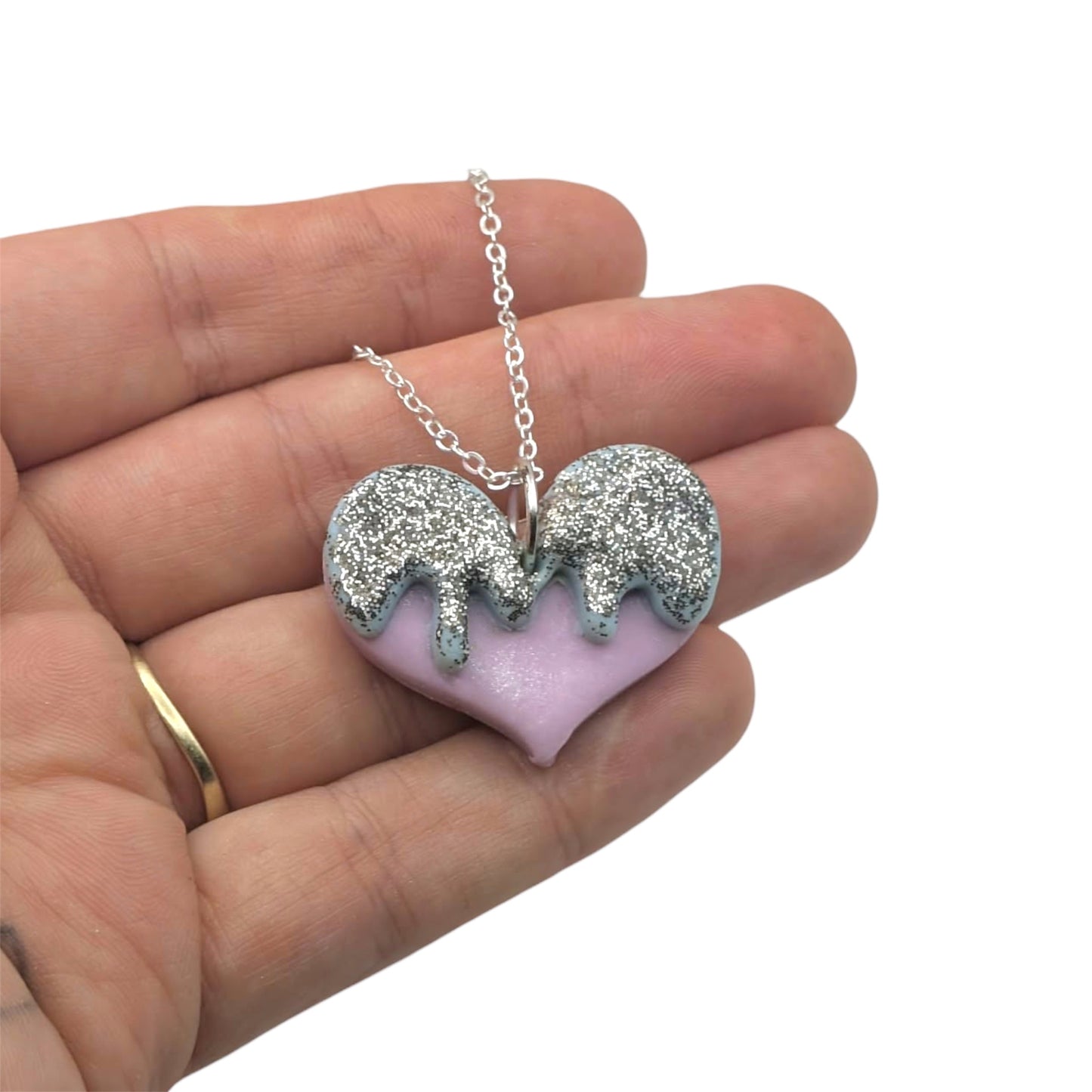 Necklace with a heart-shaped pendant featuring glittery drips held in a hand on a white background