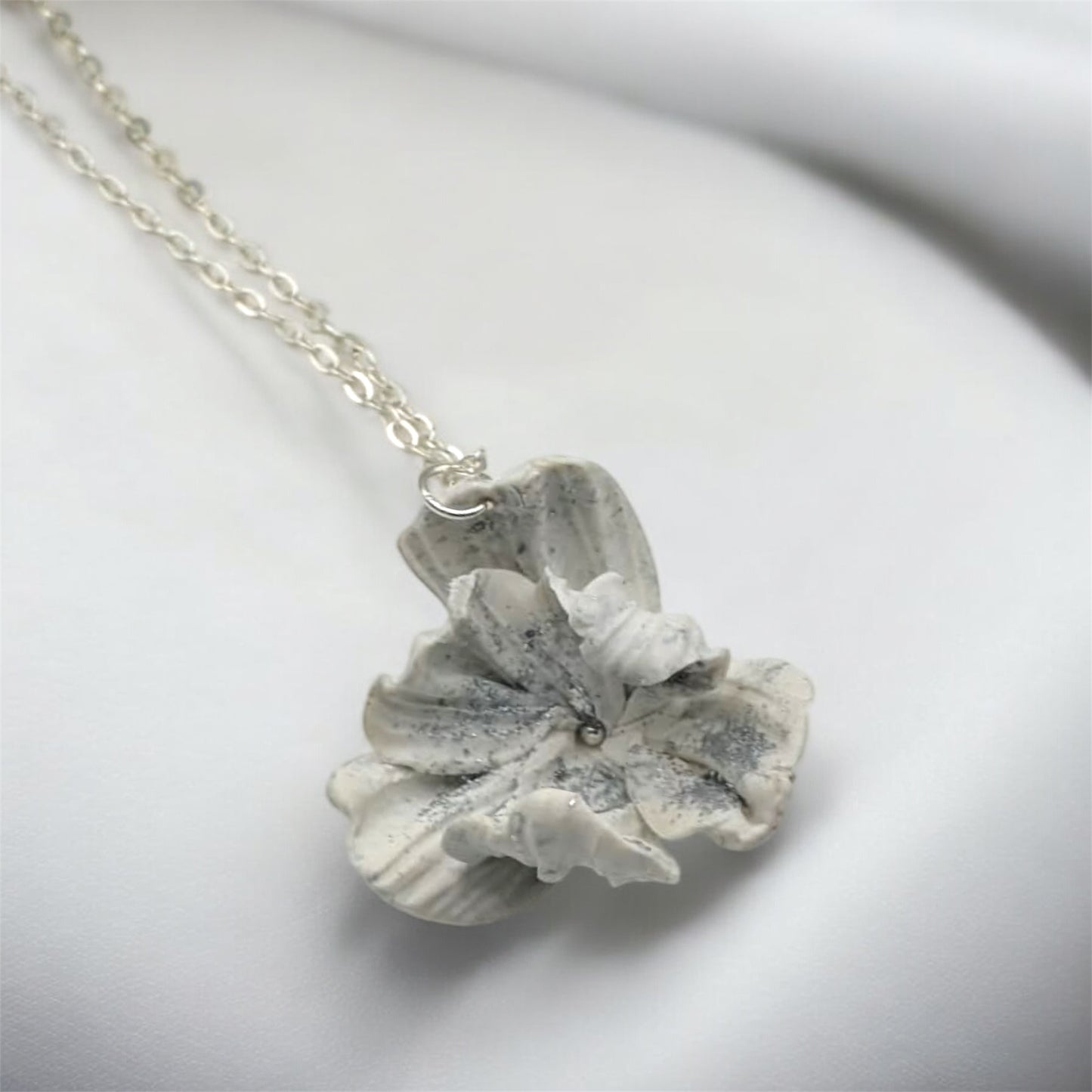 White polymer clay flower pendant with silver leaf detailing close-up